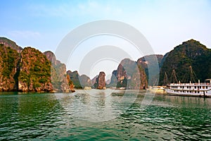 Sunset in Ha Long Bay, Vietnam. Boats, rock formations, misty mood, sunset and reflections in the South China Sea, Vietnam