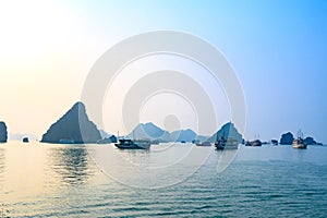 Sunset in Ha Long Bay, Vietnam. Boats, rock formations, misty mood, sunset and reflections in the South China Sea, Vietnam