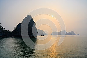 Sunset in Ha Long Bay, Vietnam. Sunset behind misty rock formations, boat in foreground, reflections in South China Sea, Vietnam