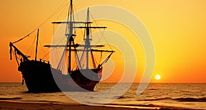 the sunset has been setting behind an old sailing vessel on the beach