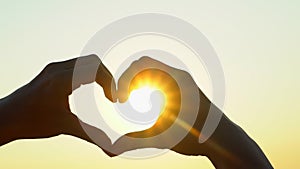 Sunset heart hands. Woman shapes heart with hands over sun on sunrise or sunset in nature summer. Male making heart