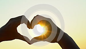 Sunset heart hands. Woman shapes heart with hands over sun on sunrise or sunset in nature summer. Male making heart