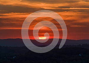 Sunset in the hilly countryside with big red sun and dramatic clouds