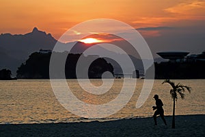 Sunset in Icarai beach with a person walking in the sand, and Ilha da Boa Viagem island in the background