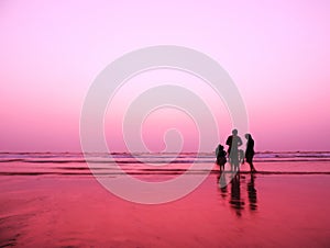 After sunset image of a beach with gentle pink purple sky color along with silhouette of a happy family with friends playing