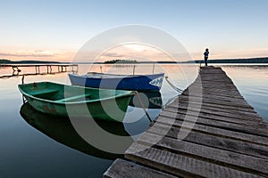 Sunset on the lake with boats and a girl standing on the pier