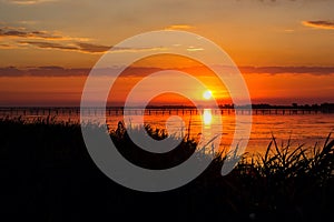 Sunset lake river landscape. Golden natural sky water sunset view of jetty or small bridge at horizon and orange sky above it with