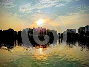 Sunset with lake surrounded by building and tree with water reflection