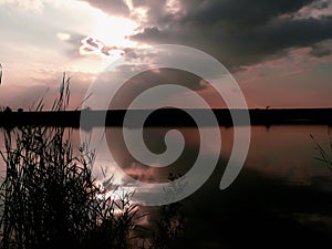 Sunset at lake, thunderclouds and grass on a shore photo