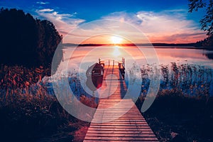 Sunset on a lake. Wooden pier with fishing boat at sunset in Finland