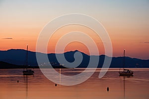 Sunset landscape of a bay with two sailboats with the mountains behind. photo
