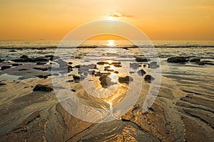 Sunset landscape with beach, sun and stones at sea shore