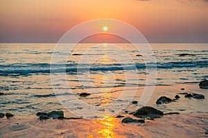 Sunset landscape with beach, sun and stones at sea shore