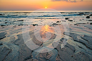 Sunset landscape with beach, sun and stones at sea shore