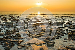 Sunset landscape with beach, sun and stones at sea shore