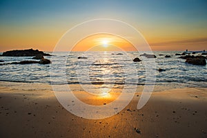 Sunset landscape with beach, sun and stones at sea shore