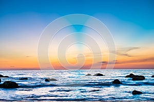 Sunset landscape with beach, sun and stones at sea shore