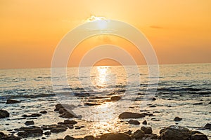 Sunset landscape with beach, sun and stones at sea shore