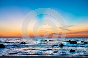 Sunset landscape with beach, sun and stones at sea shore