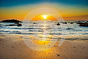 Sunset landscape with beach, sun and stones at sea shore