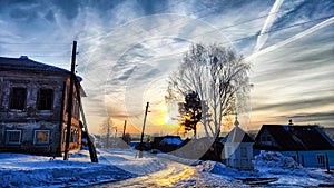 Sunset landscape in the countryside in winter. The setting sun behind the roof of the house in the evening. The disk of