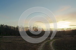 Sunset landscape with field, road and sun, russian country