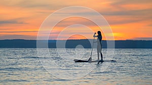 Sunset landscape with a gorgeous lady floating on a paddleboard. Freedom concept.