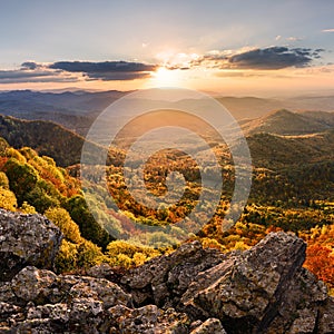 Sunset landscape with high peaks and valley with autumn spruce forest under vibrant colorful evening sky in forest mountains