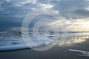 Sunset with Light Beams over the Ocean with Foamy Waves on the Beach