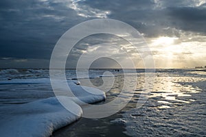 Sunset with Light Beams over the Ocean with Foamy Waves on the Beach