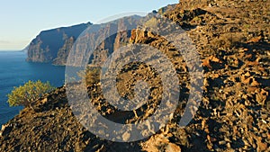 Sunset light illuminate steep Los Gigantes cliifs rocky barren volcanic mountains with dark blue deep ocean water. Sea