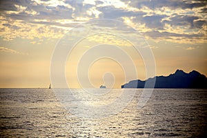 Sunset light on an isolated sailboat, sailing on the horizon, with the coast in backlight, under a dramatic sky