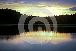 Sunset light over dark forest trees behind lake waters