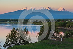 Sunset lighting Kluchevskaya group of volcanoes with reflection in river Kamchatka.