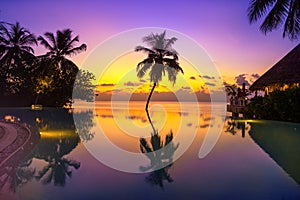 Sunset on Maldives island, luxury water villas resort and wooden pier. Beautiful sky and clouds and beach with palms background