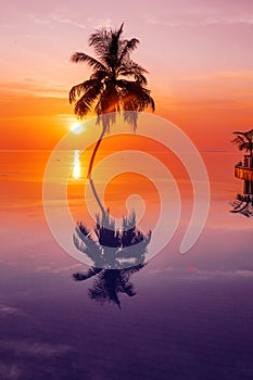 Sunset on Maldives island, luxury water villas resort and wooden pier. Beautiful sky and clouds and beach with palms background