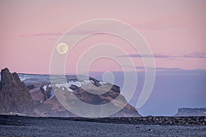 Sunset and moon rise over mountains and Vikâ€™s black sand beach in Iceland