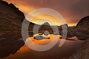 Sunset in mountains near lake. Sunlight reflected on mountain tops. Golden light from sky reflected in a mountain lake. Ergaki.