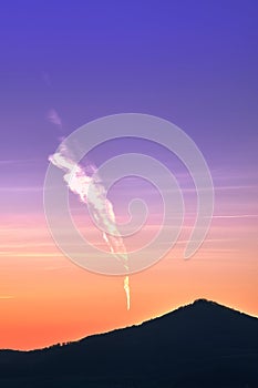 Sunset in the mountains with a trail of a plane and clouds