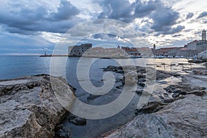 Sunset and Night view of Dubrovnik old town from seaside with reefs in foreground, Croatia