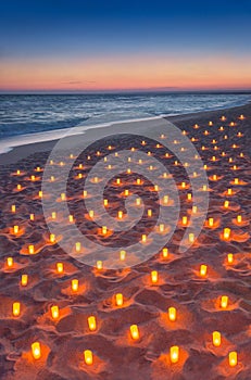 Sunset ocean sandy beach decorated with lot flare lights of candles. Romantic sea vacation or honeymoon concept vertical