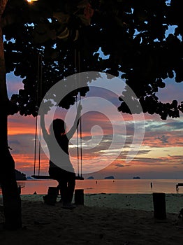 Sunset by the ocean. Silhouettes of a girl riding a swing