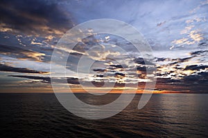 Sunset in the open ocean. Colorful views of the surface of the water and the sky with clouds over ocean.