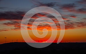 A sunset with orange clouds with silhouette wind turbines on the horizon