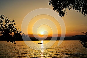 Sunset on an orange-gold sky, a boat floating in the water