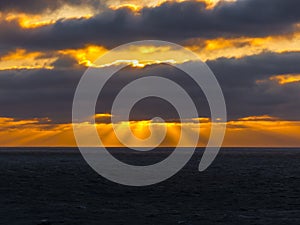 Sunset over the Atlantic ocean with sun breaking trough clouds.