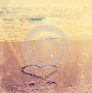 Sunset over beach on shore with love heart in the sand