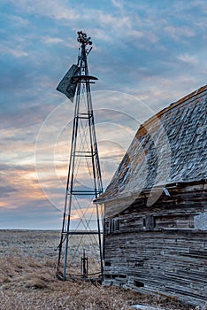 Sunset over a broken vintage windmill beside an old barn in Saskatchewan