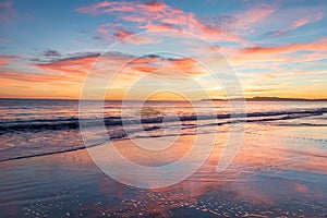 Sunset over coast with saturated colors in the sky and reflections in the water.