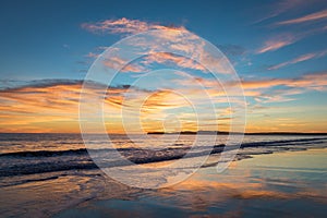 Sunset over coast with saturated colors in the sky and reflections in the water.